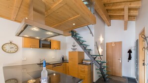 A modern kitchen with wooden cabinets, a stainless steel range hood, and a glass staircase. - Waldbort Penthouse (Wengen)