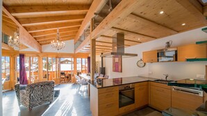 A modern kitchen with wooden cabinets, a large island, and a dining area with a zebra-patterned sofa. - Waldbort Penthouse (Wengen)