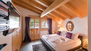 A bedroom with a large bed, wooden ceiling beams, a TV, and a window with curtains. - Waldbort Penthouse (Wengen)