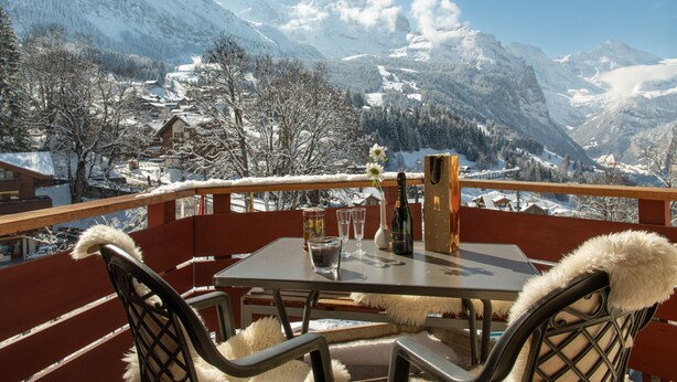 A table with a bottle, glasses, and a bag on a balcony with a mountain view.