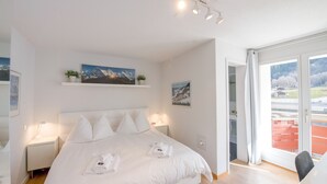 A modern hotel room with a large bed, bedside lamps, a mounted picture, and a view of a red building through the window.