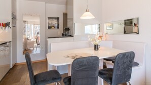 A modern kitchen with white cabinets, a dining table with four chairs, and a hanging pendant light.