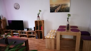 A living room with a wooden floor, a TV, a bookshelf, a table with purple cushions, and a painting on the wall. - 2 bedroom apartment in neuburg steinhausen (Neuburg Steinhausen)