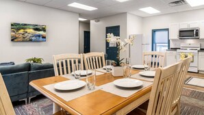 Un comedor con una mesa de madera dispuesta para cuatro personas, rodeada de sillas, y una cocina al fondo.