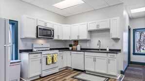 Una cocina moderna con armarios blancos, un microondas de acero inoxidable, una estufa a gas y un lavamanos.