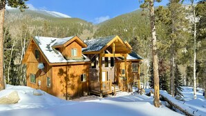 Una cabaña de madera con balcón, rodeada de nieve y árboles.