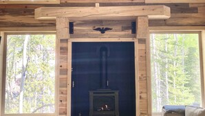 Interior de una cabaña de madera con chimenea, ventanas amplias y un sofá.