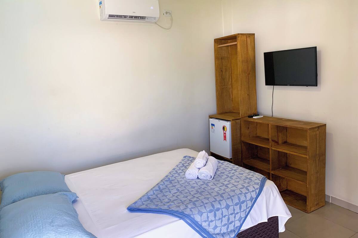 A bedroom with a bed, a TV mounted on the wall, a small refrigerator, and a wooden cabinet.