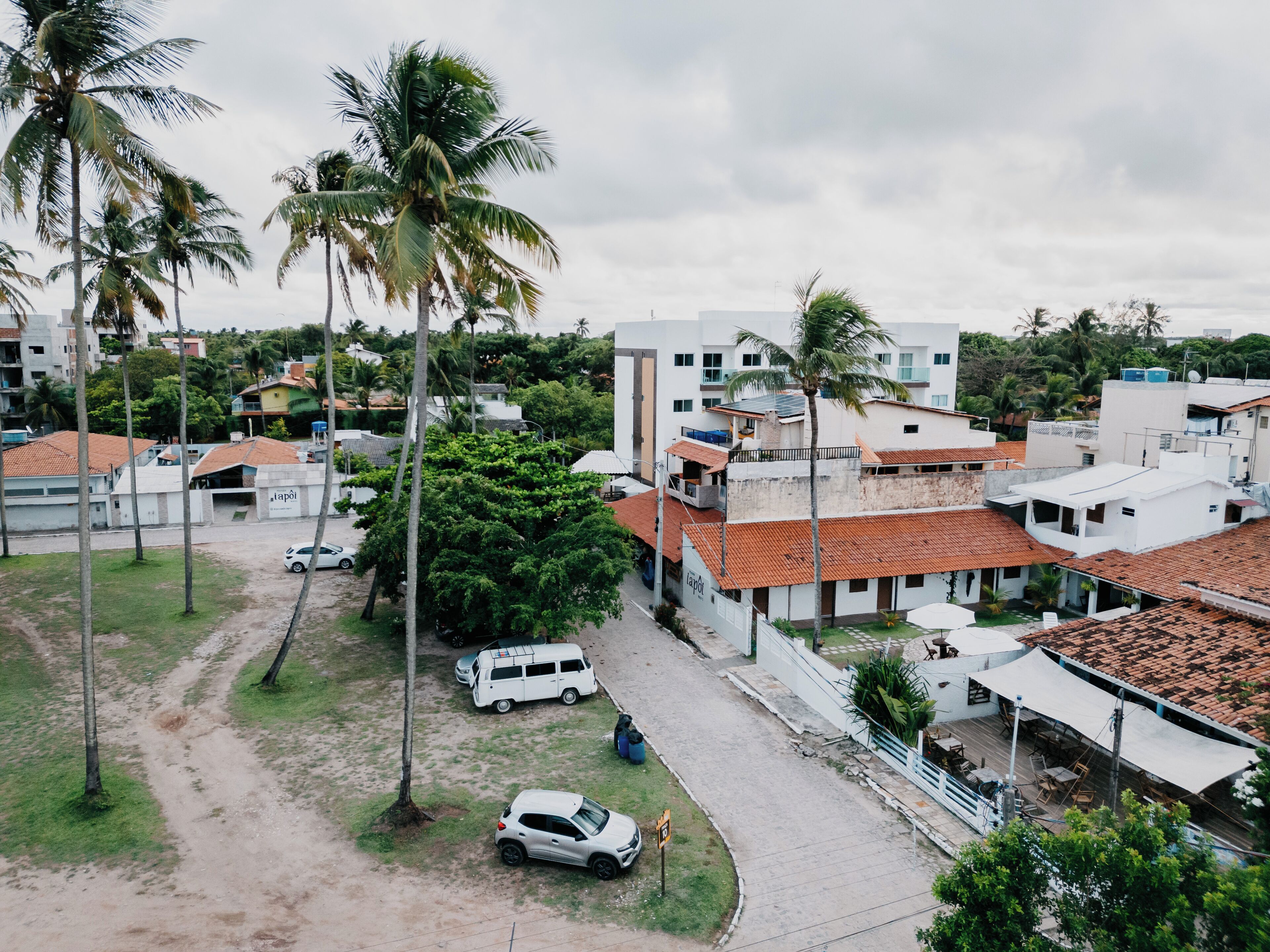 Vue aérienne d’un quartier résidentiel avec des maisons, des palmiers et un chemin de terre.