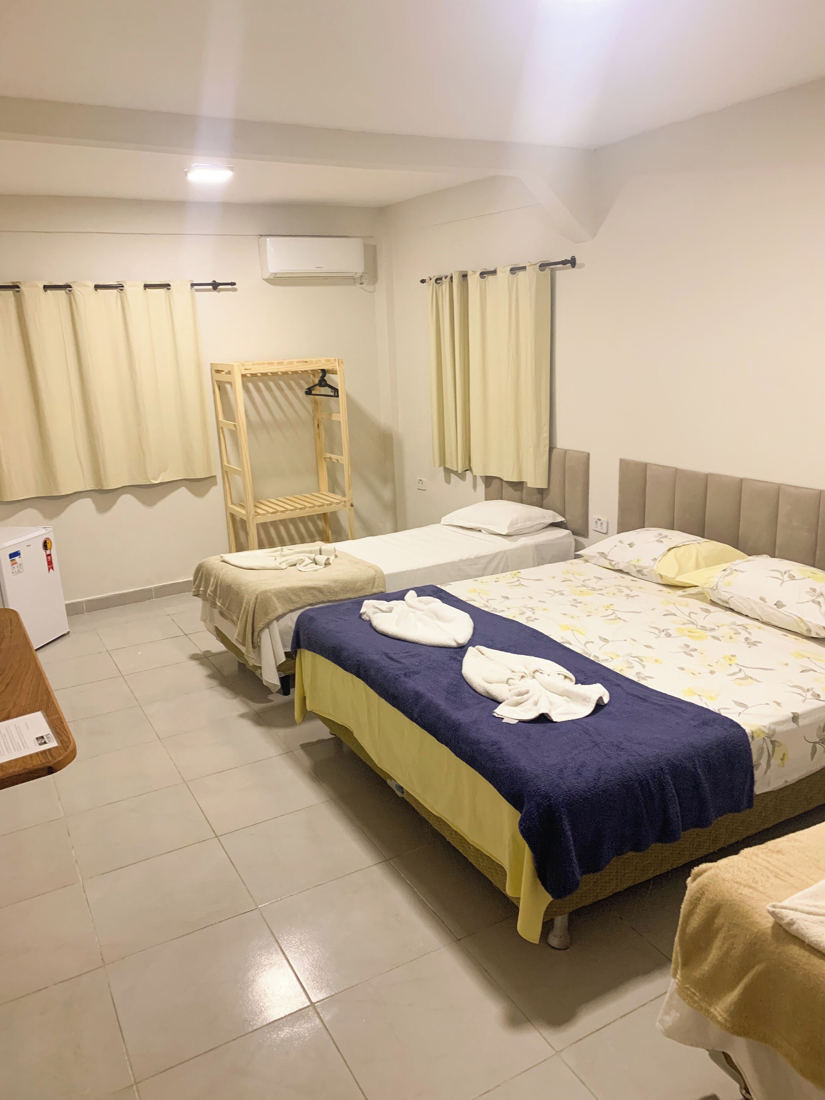 A hotel room with two beds, a wooden wardrobe, a mirror, and a small table.