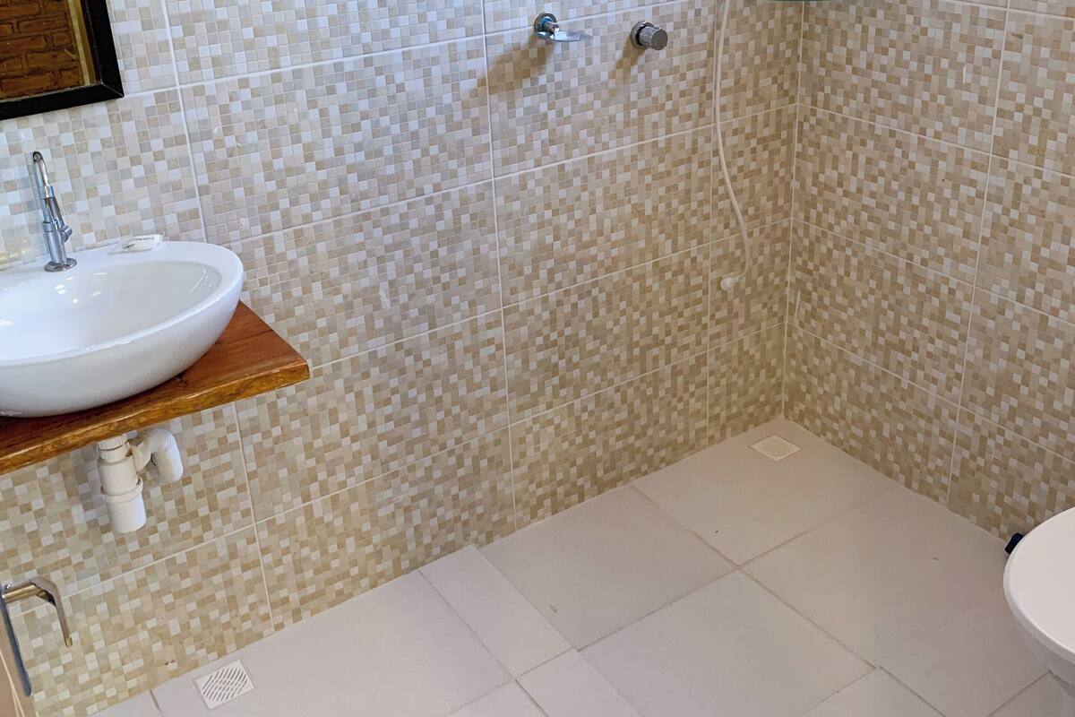 A bathroom with a tiled mosaic wall, a white sink with a wooden countertop, a glass shower enclosure, and a white toilet.
