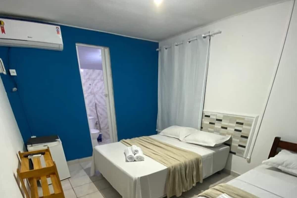A hotel room with two beds, a small desk, a chair, and a window with curtains.