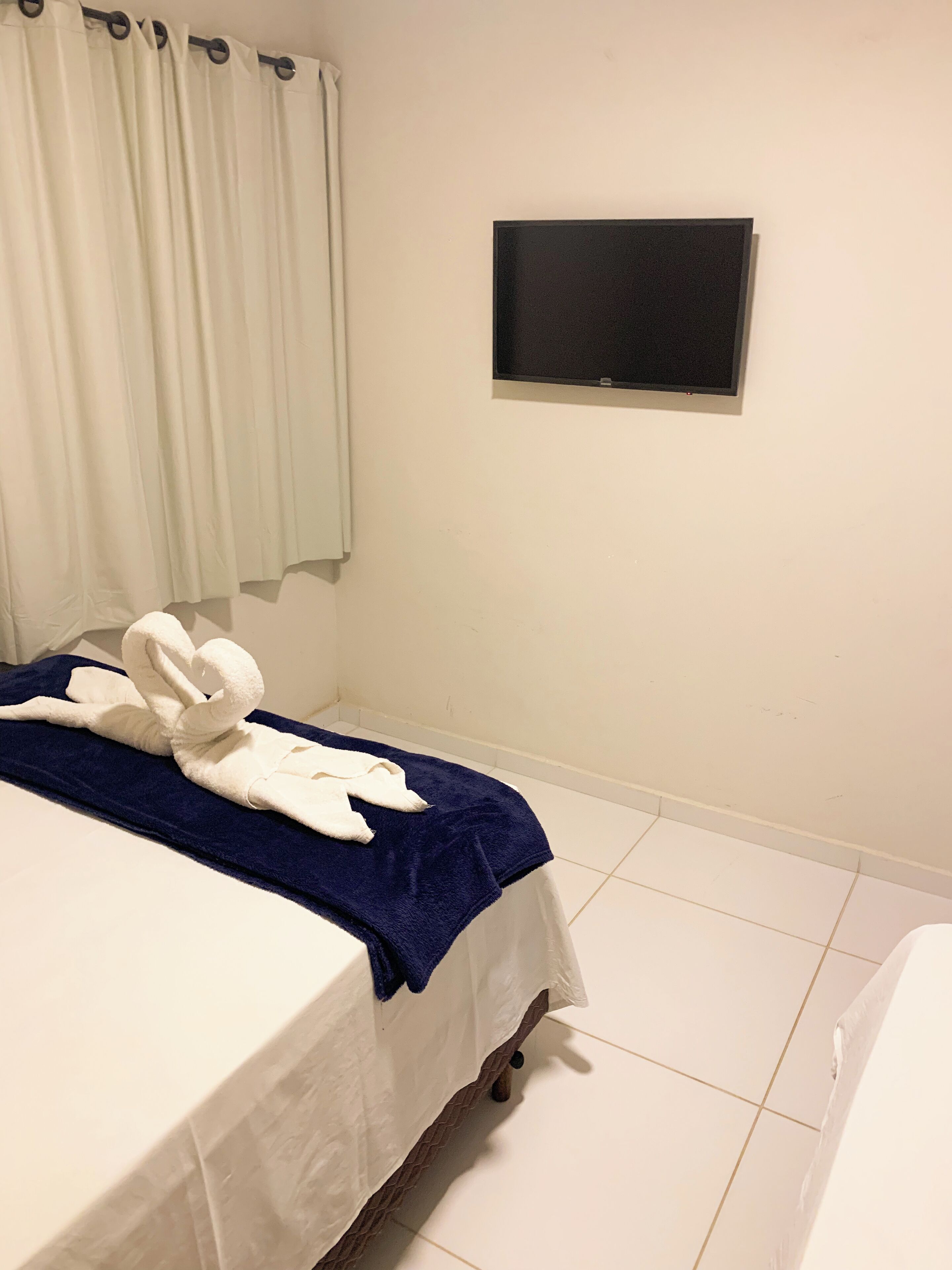 A hotel room with a bed, a TV mounted on the wall, and a window with curtains.