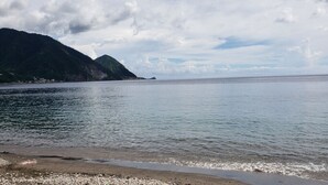 Mar calmo com uma praia e montanhas ao fundo.
