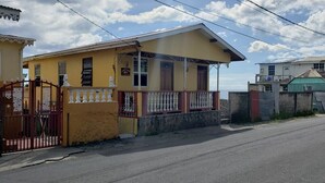 Um edifício amarelo com varanda, portão de entrada e rua ao fundo.