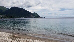 A calm sea with a pebbled beach and mountains in the background. - Roseau Hostel & Beach Front Property 12 (Roseau)