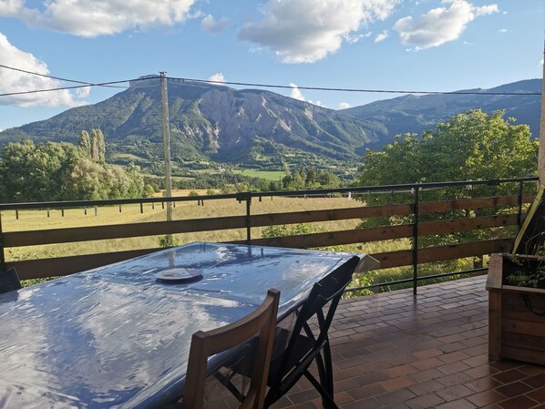 A table with a glass top and a chair, overlooking a mountainous landscape with a wooden fence and a power line.