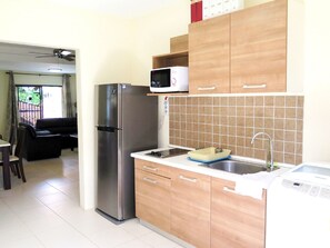 A compact kitchen with a stainless steel refrigerator, wooden cabinets, a microwave, and a sink.