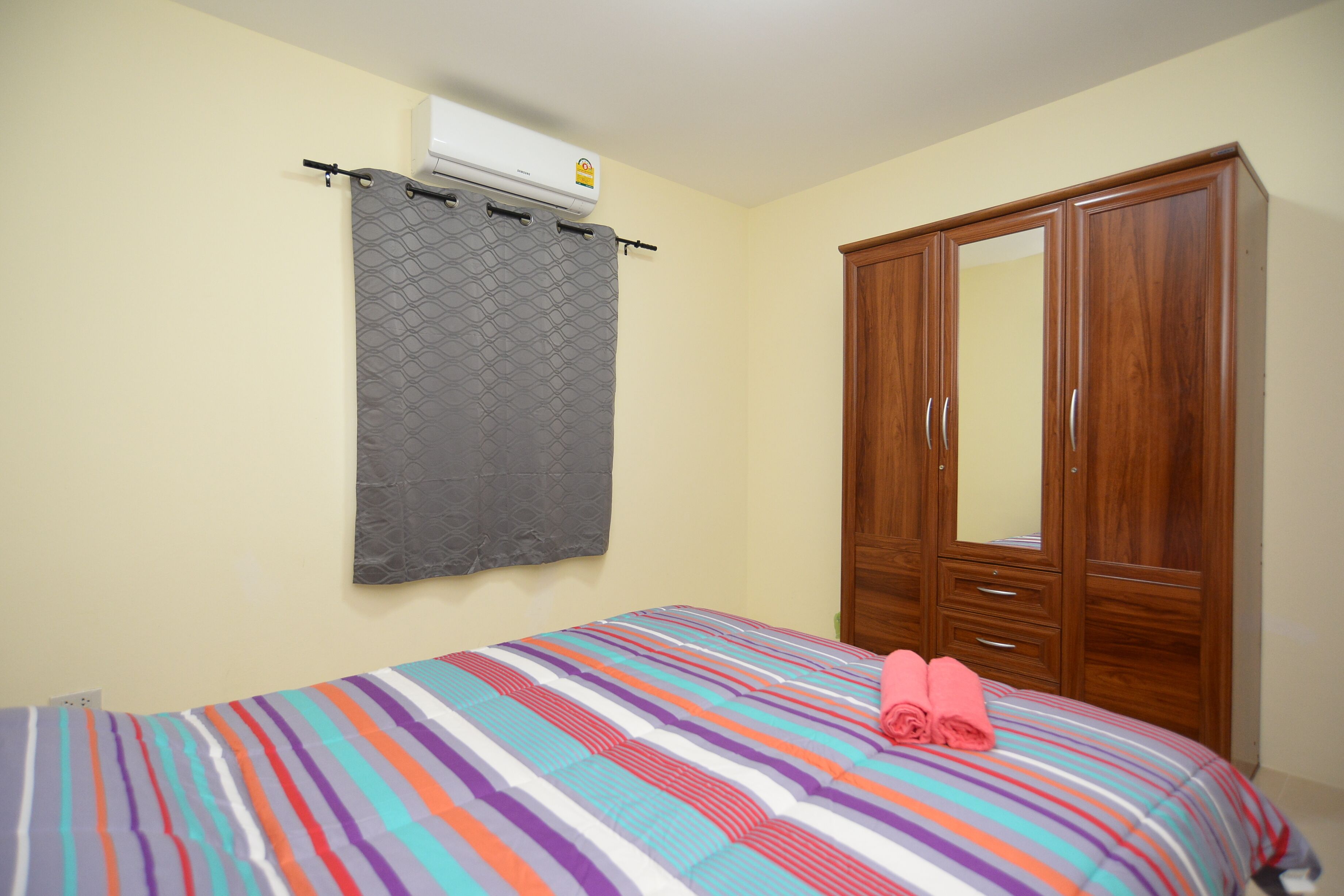 Un dormitorio con cama, cortina gris, armario de madera y aire acondicionado instalado en la pared.