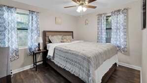 Een slaapkamer met een bed, nachtkastje, plafondventilator en behangen gordijnen.