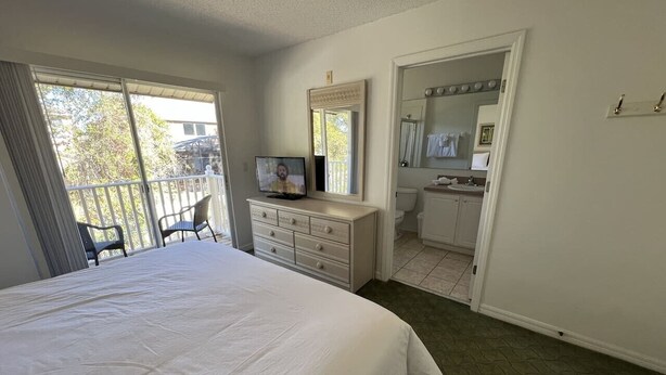 Ein Schlafzimmer mit einem großen Bett, einem Schminktisch, einem Fernseher, einem Badezimmer mit Spiegel und einem Balkon.