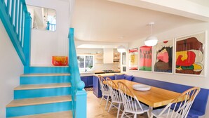 A modern kitchen with a wooden island, blue staircase, and white chairs. - ⟰ DELIGHTFULLY DESIGNED (Boyne City)