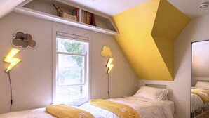 A bedroom with two beds, a sloped ceiling, a window, and a mirror. - ⟰ DELIGHTFULLY DESIGNED (Boyne City)