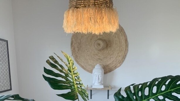 A dining table with a clear glass vase, surrounded by woven placemats, and large green monstera leaves.