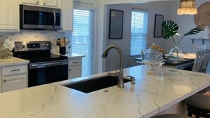A modern kitchen with white cabinetry, a marble countertop, a stainless steel range, and a black oven.