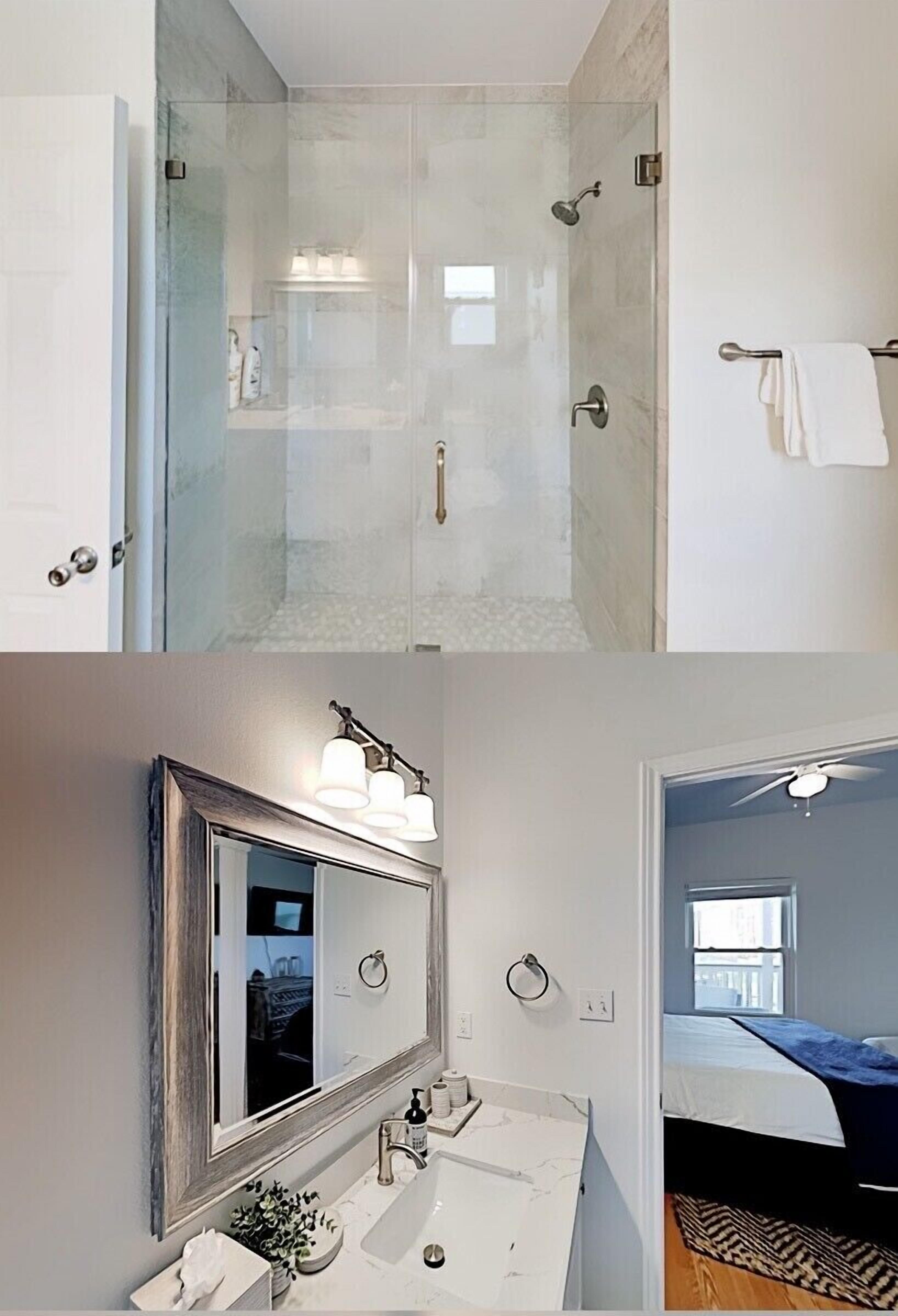 A modern bathroom with a glass shower enclosure, a large mirror with wall-mounted lights, and a visible towel rack.