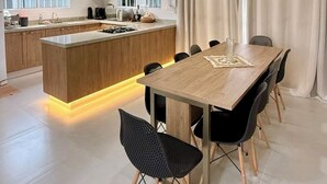Eine moderne Küche mit Kochinsel, Essbereich mit Holztisch und -stühlen sowie ein großes Fenster mit Vorhängen.