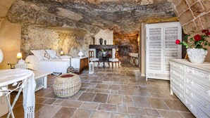 Ein rustikaler Raum mit Steinwänden, einem Bett, einem Esstisch, Stühlen und einem weißen Schrank.