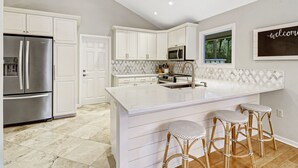 Een moderne keuken met witte kastjes, een roestvrijstalen koelkast, een magnetron en een groot eiland met barkrukken.