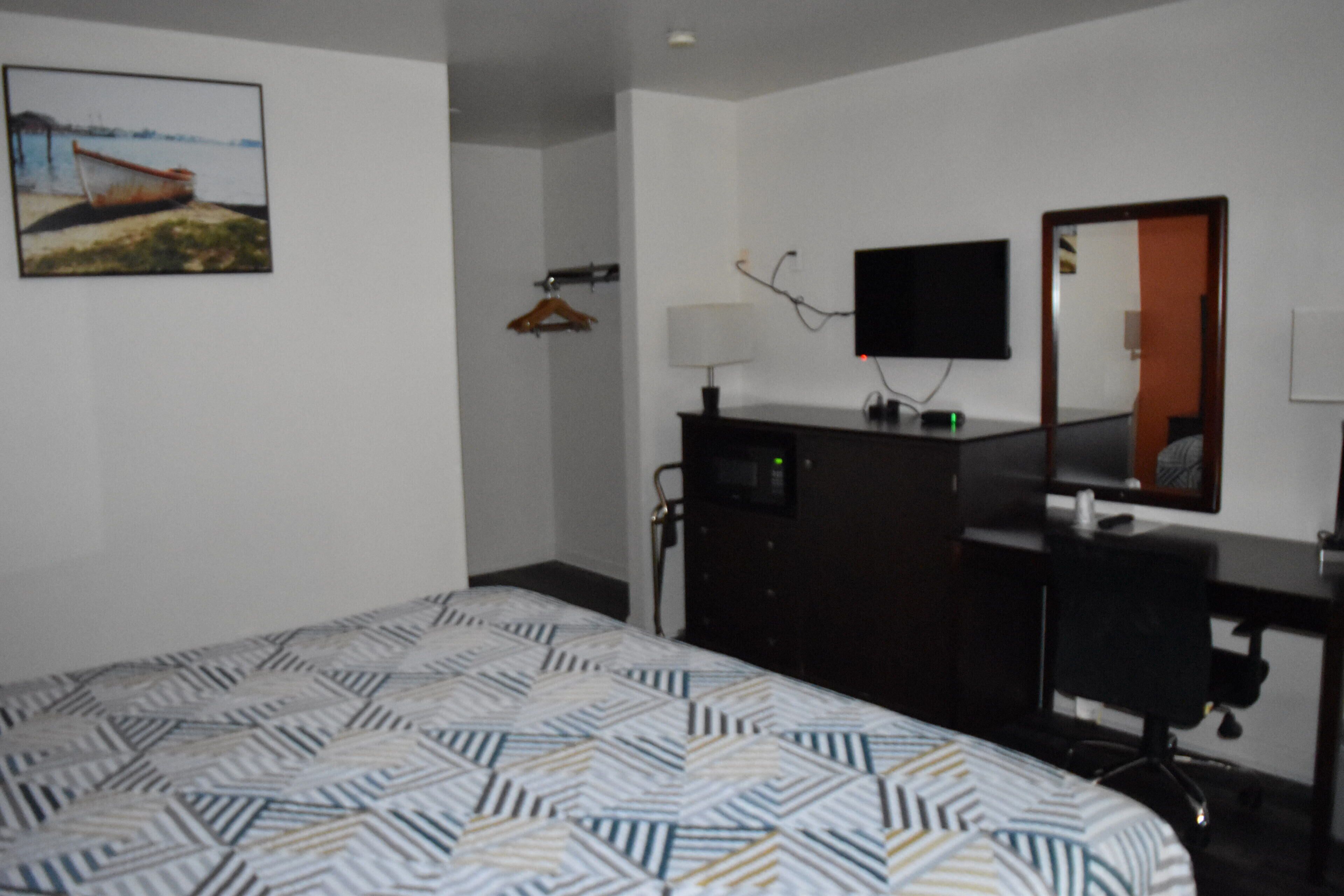 Ein Hotelzimmer mit einem Bett, einem Schminktisch, einem Spiegel, einem Fernseher und einem Bild an der Wand.