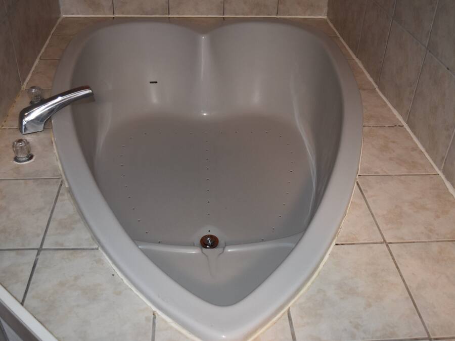 A heart-shaped bathtub with a single faucet and a drain.
