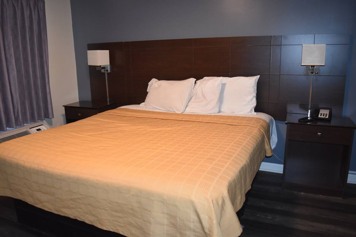 A hotel room with a large bed, two bedside tables, a headboard, and a wall-mounted lamp.