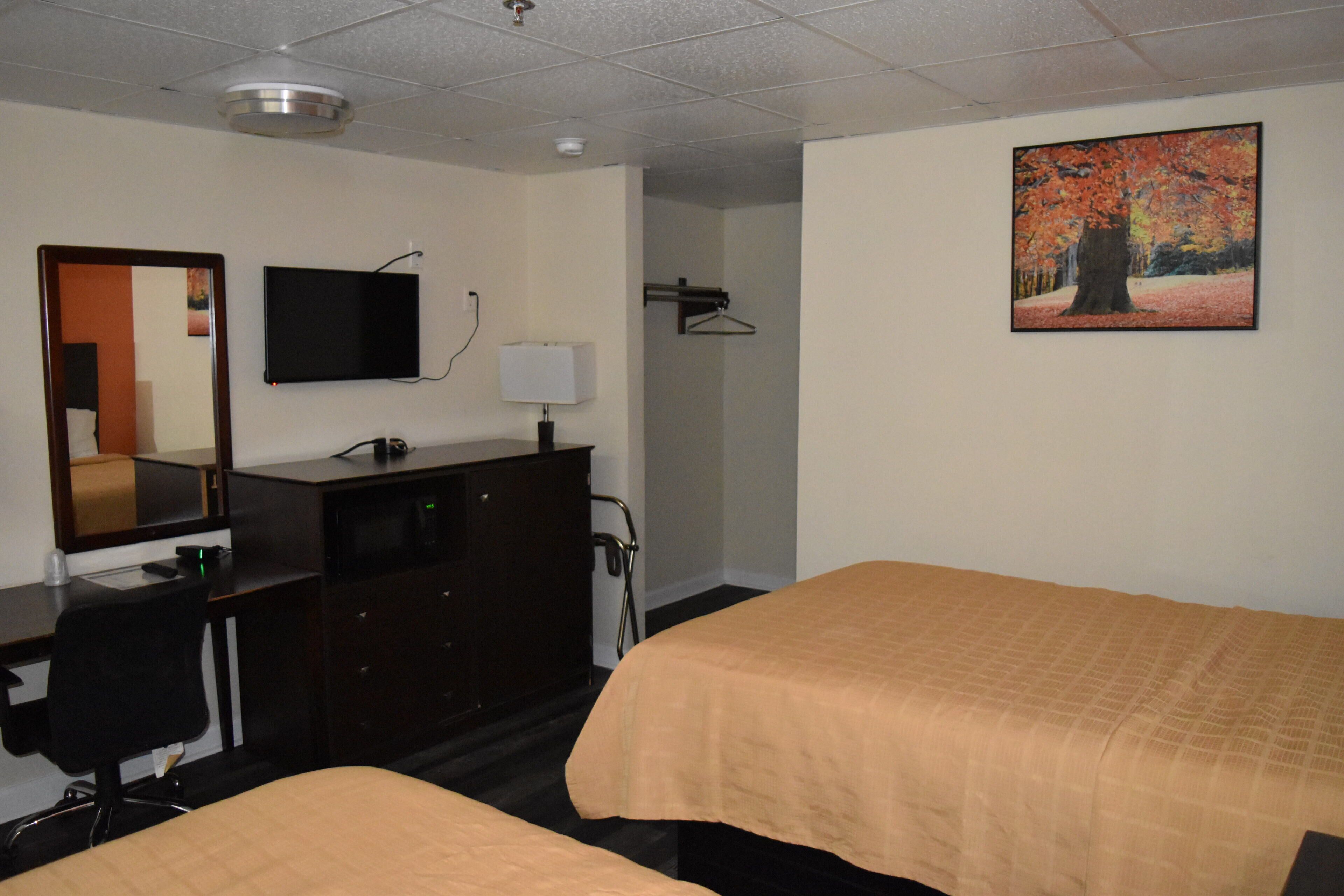 Quarto de hotel com duas camas, uma escrivaninha, cômoda, televisão, um quadro e um espelho.