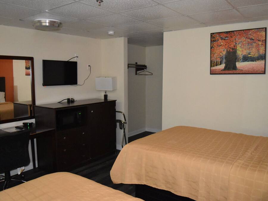 A hotel room with two beds, a desk, a dresser, a television, a painting, and a mirror.