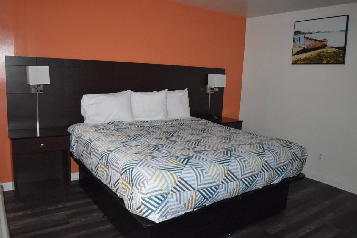 A bedroom with a bed, two bedside tables, a headboard, and a wall-mounted picture.