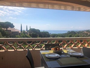 A balcony with a table set for two, overlooking a scenic view of the sea and distant buildings.