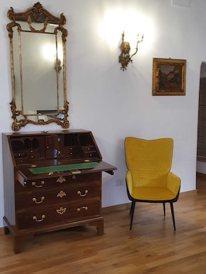Quarto com escrivaninha de madeira, cadeira amarela, espelho grande e quadro pendurado na parede.