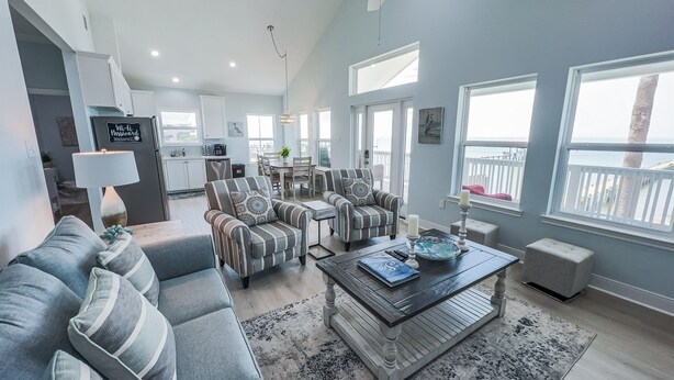 A spacious living room with a sofa, armchairs, and a coffee table. There is a kitchen area with a refrigerator and a dining table. - Waterfront Bay Views | Beautiful Private Pier (San Leon)