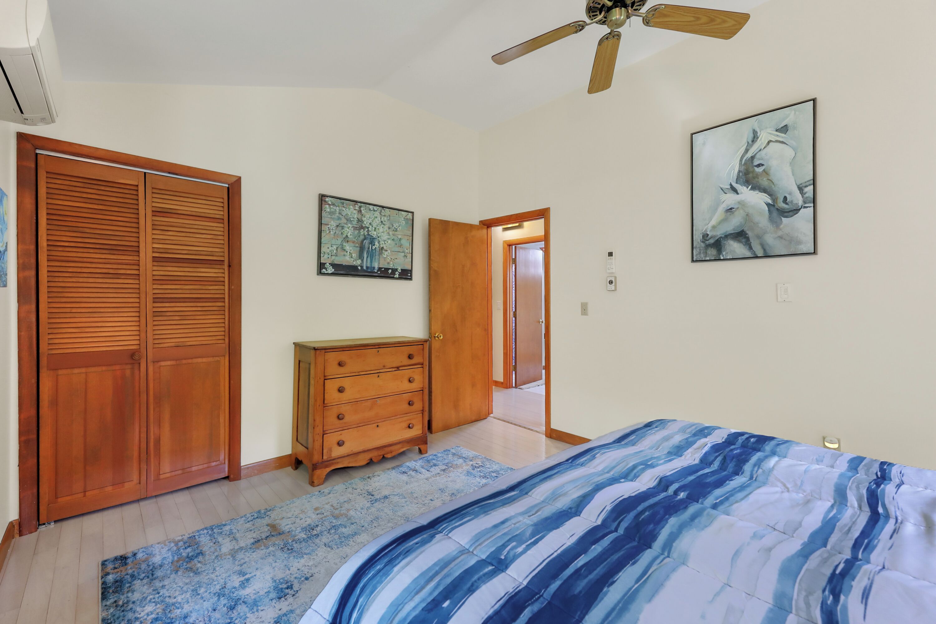A bedroom with a bed, wooden wardrobe, dresser, and artwork on the walls.