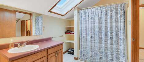 A bathroom with a skylight, a sink, wooden cabinets, and a patterned shower curtain.