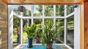A conservatory with large windows, a blue patterned rug, and potted plants.