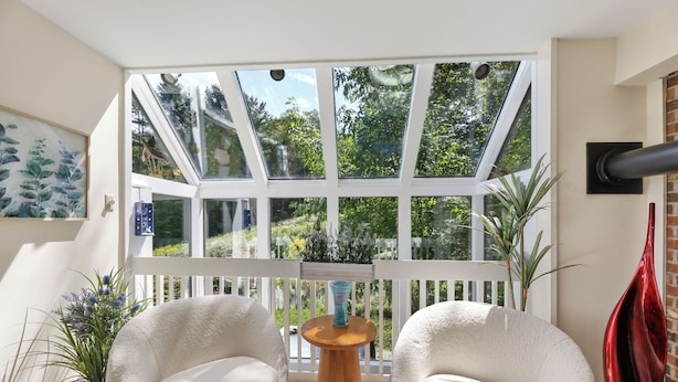 A sunlit room with a large glass window, two white armchairs, a wooden table, and a red vase.