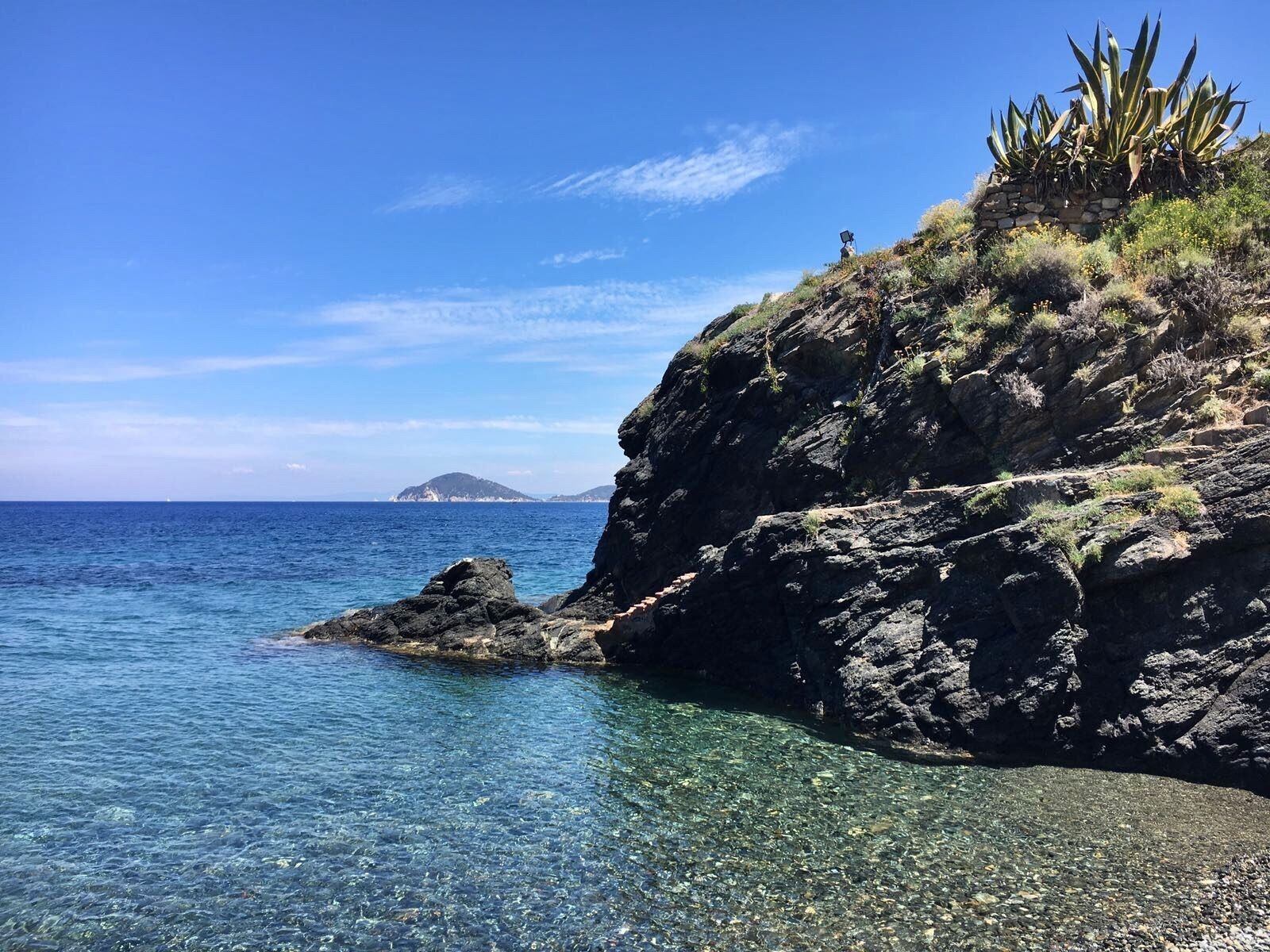 A rocky coastline with clear water and a distant island.