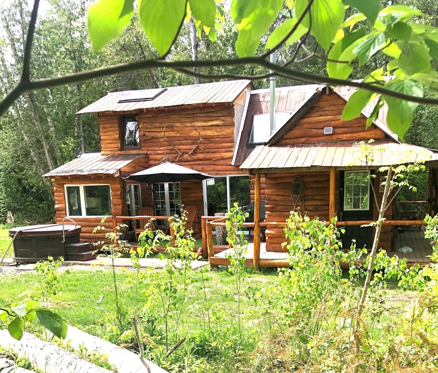 A rustic log cabin with a patio area, outdoor seating, and a hot tub.
