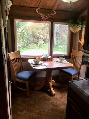 Una mesa de comedor de madera con dos sillas, un ventanal con vistas a zonas verdes y una lámpara en el techo.