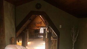 Una habitación acogedora con una cama, una silla y una mesita pequeña. El techo es de madera y en la pared hay un adorno con motivos de árbol.